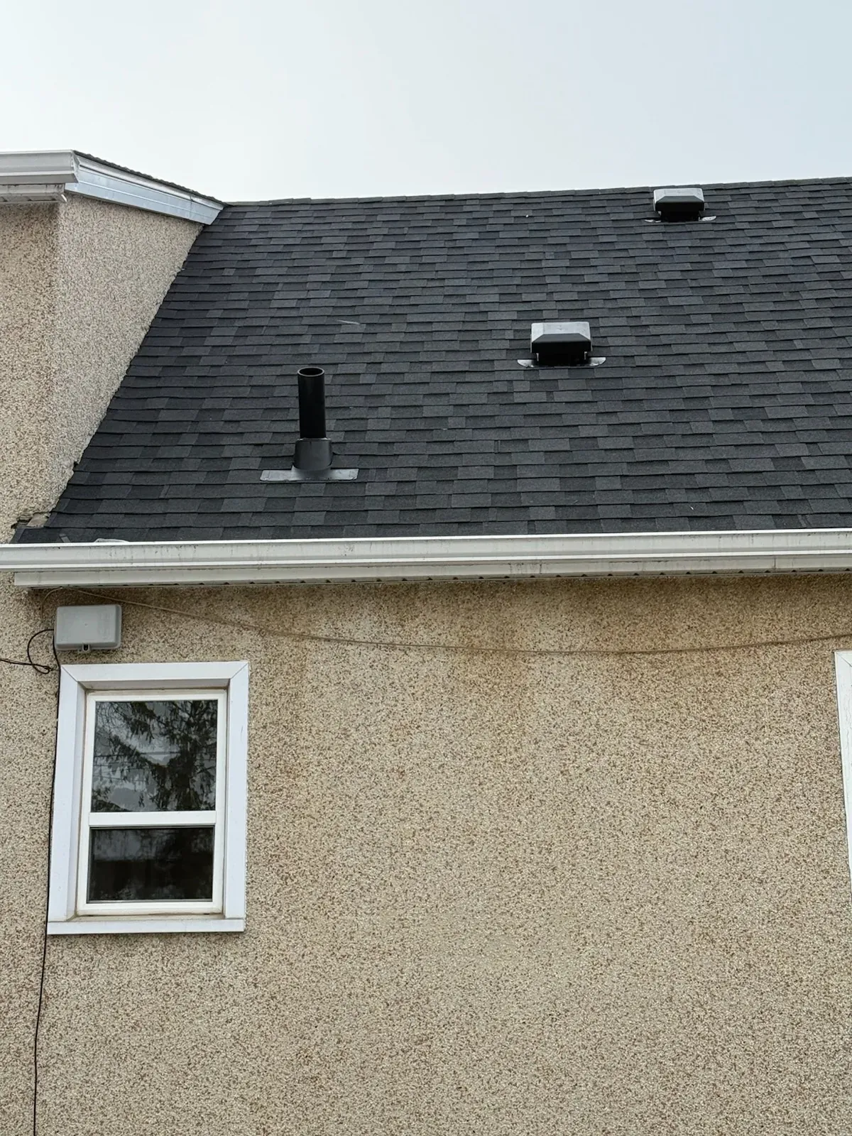 Close-up detail of a dark shingle roof against stucco