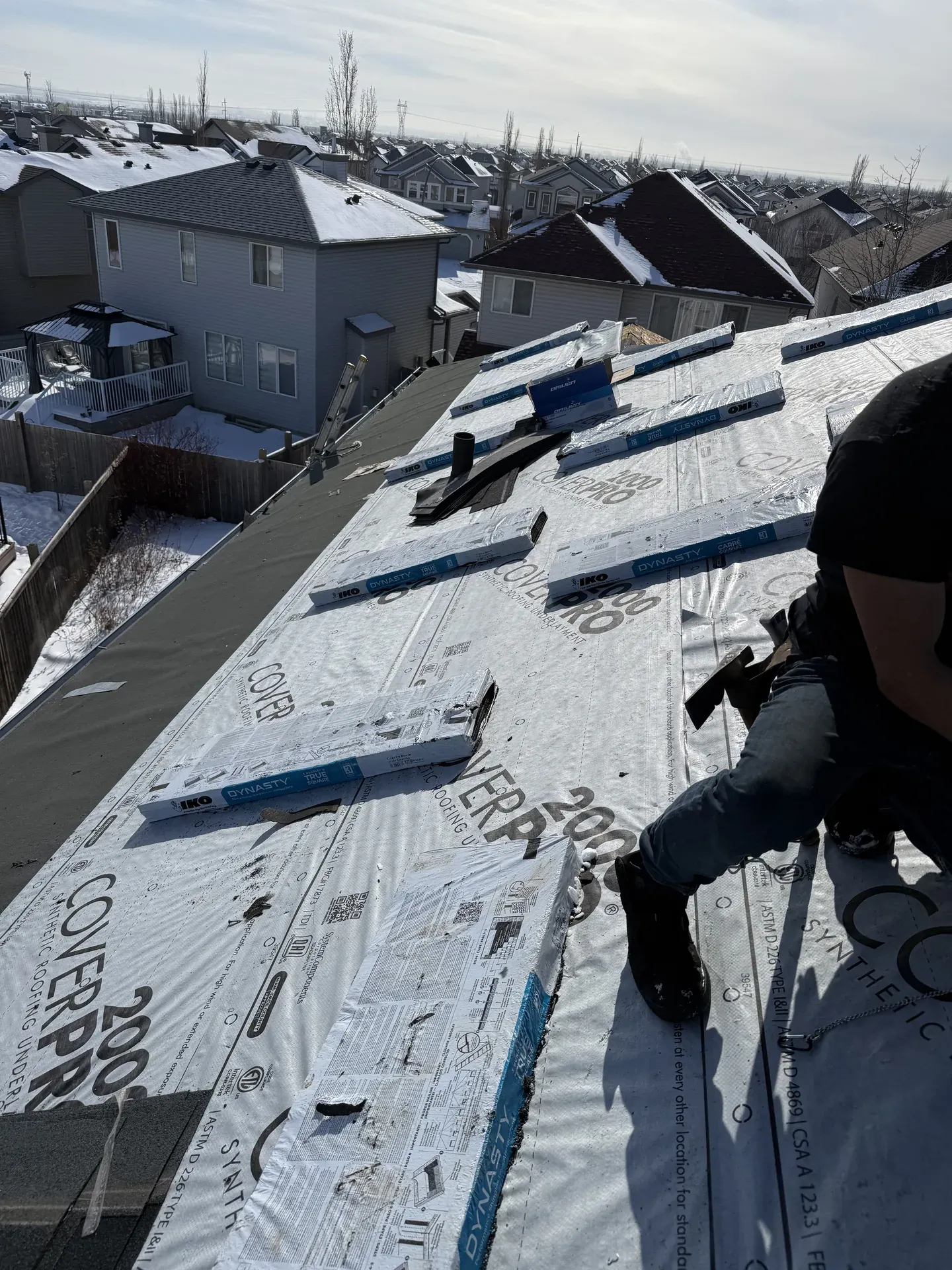 Worker laying synthetic underlayment on a roof in winter